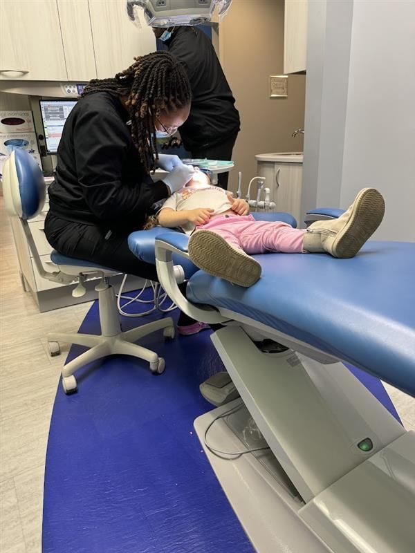 A dentist is examining a little girl's teeth in a dental office.