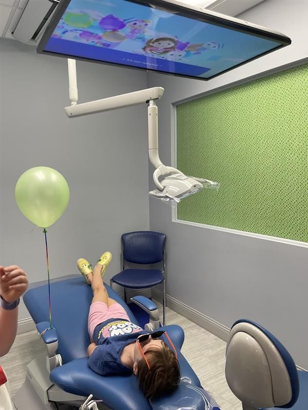 A child is laying in a dental chair with a balloon and a television.