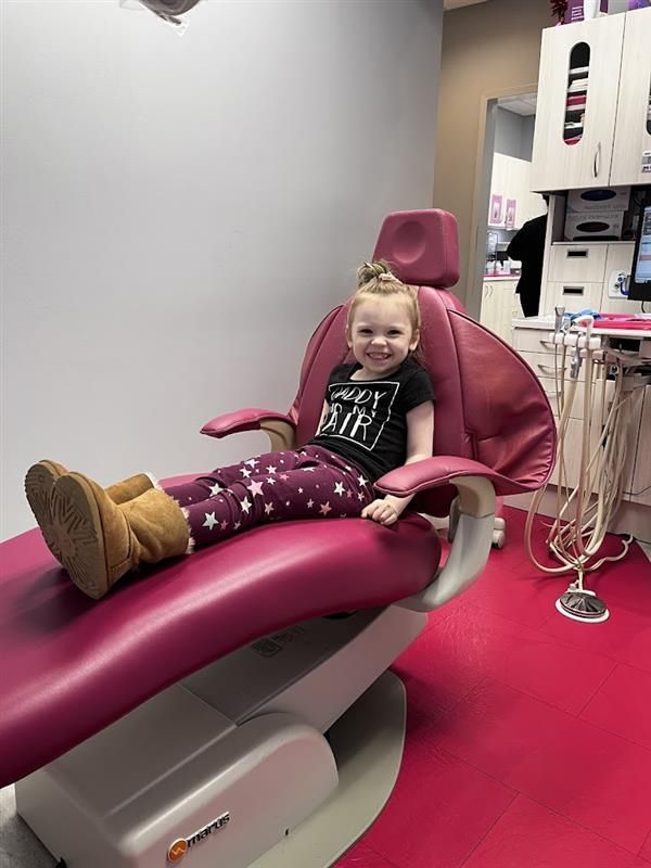 A little girl is sitting in a pink dental chair.