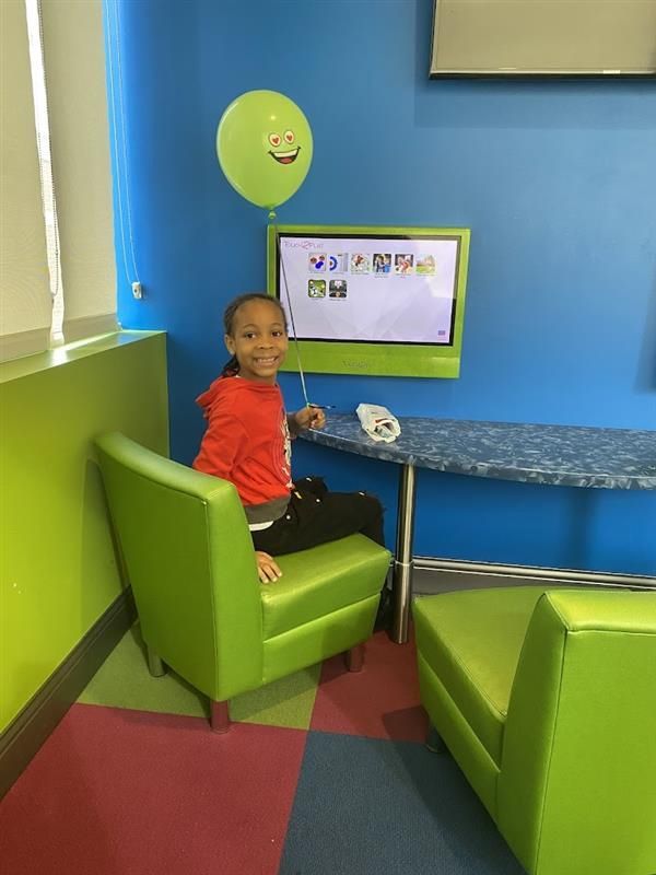 A little girl is sitting in a green chair in front of a television.