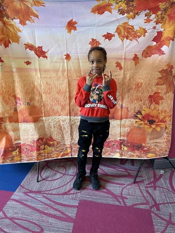 A young girl is standing in front of a fall background.