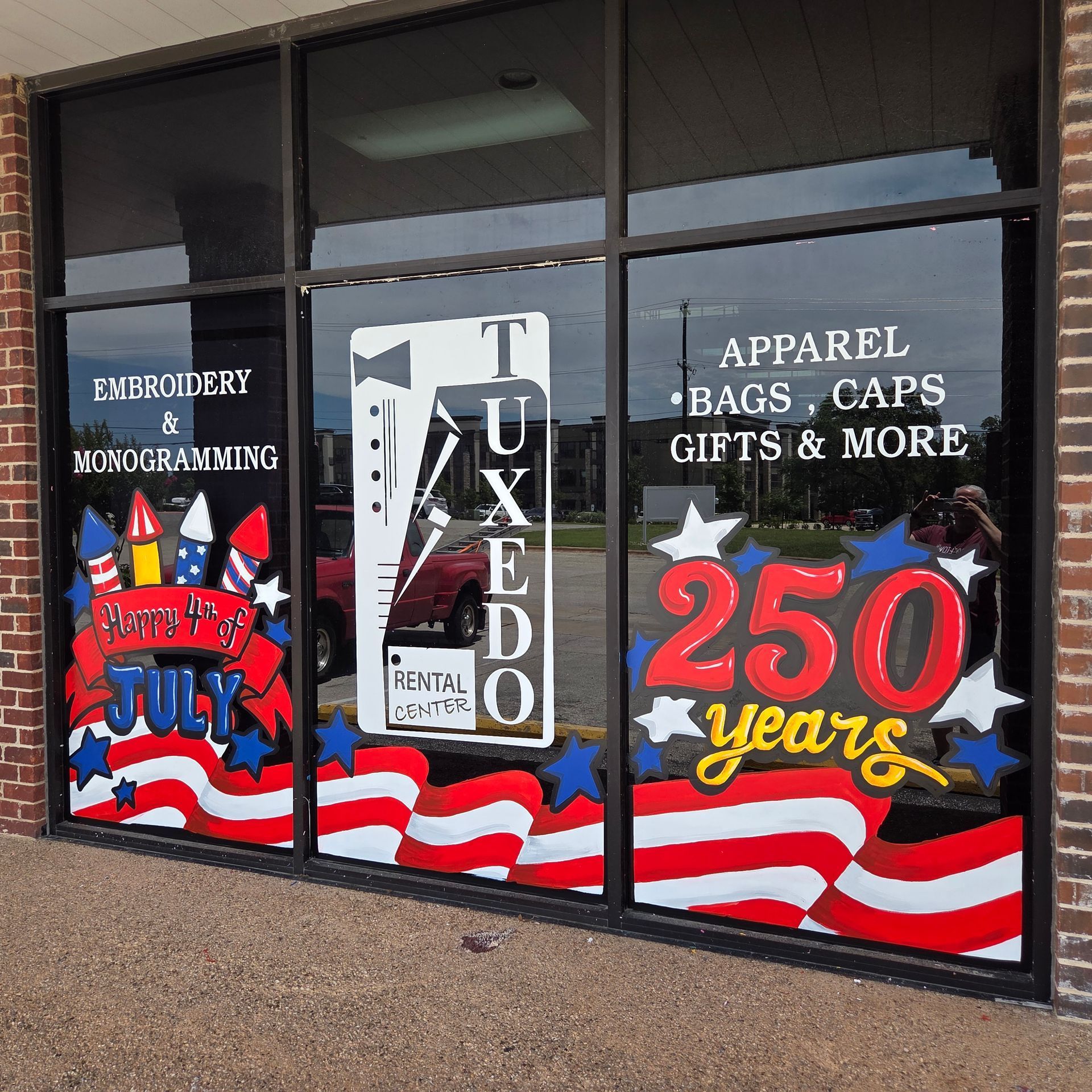 Storefront windows with patriotic red, white, and blue 250 years anniversary graphics and business signs