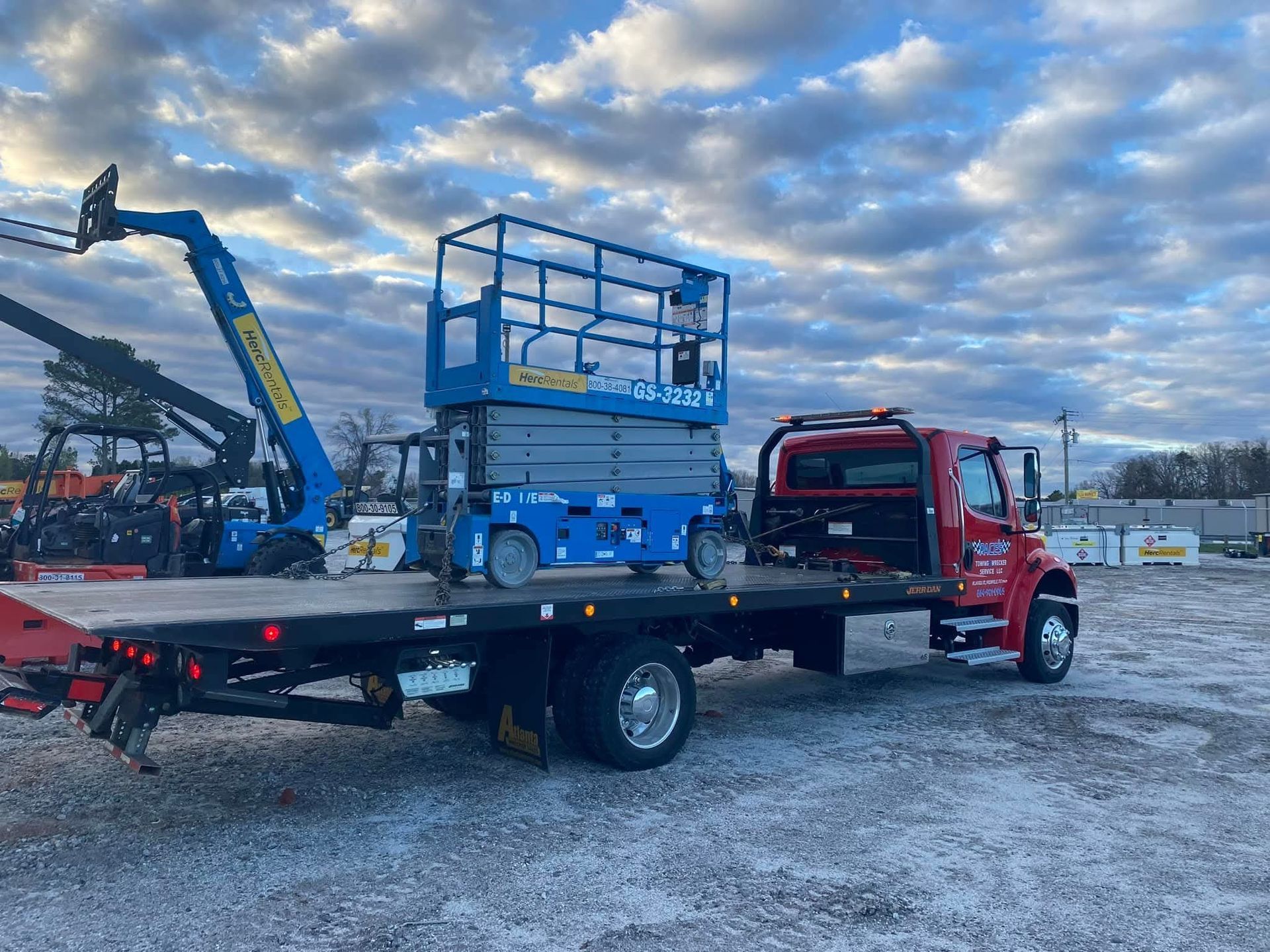 Tow truck carrying a black and gray pickup truck on a roadside, mountains in the background.