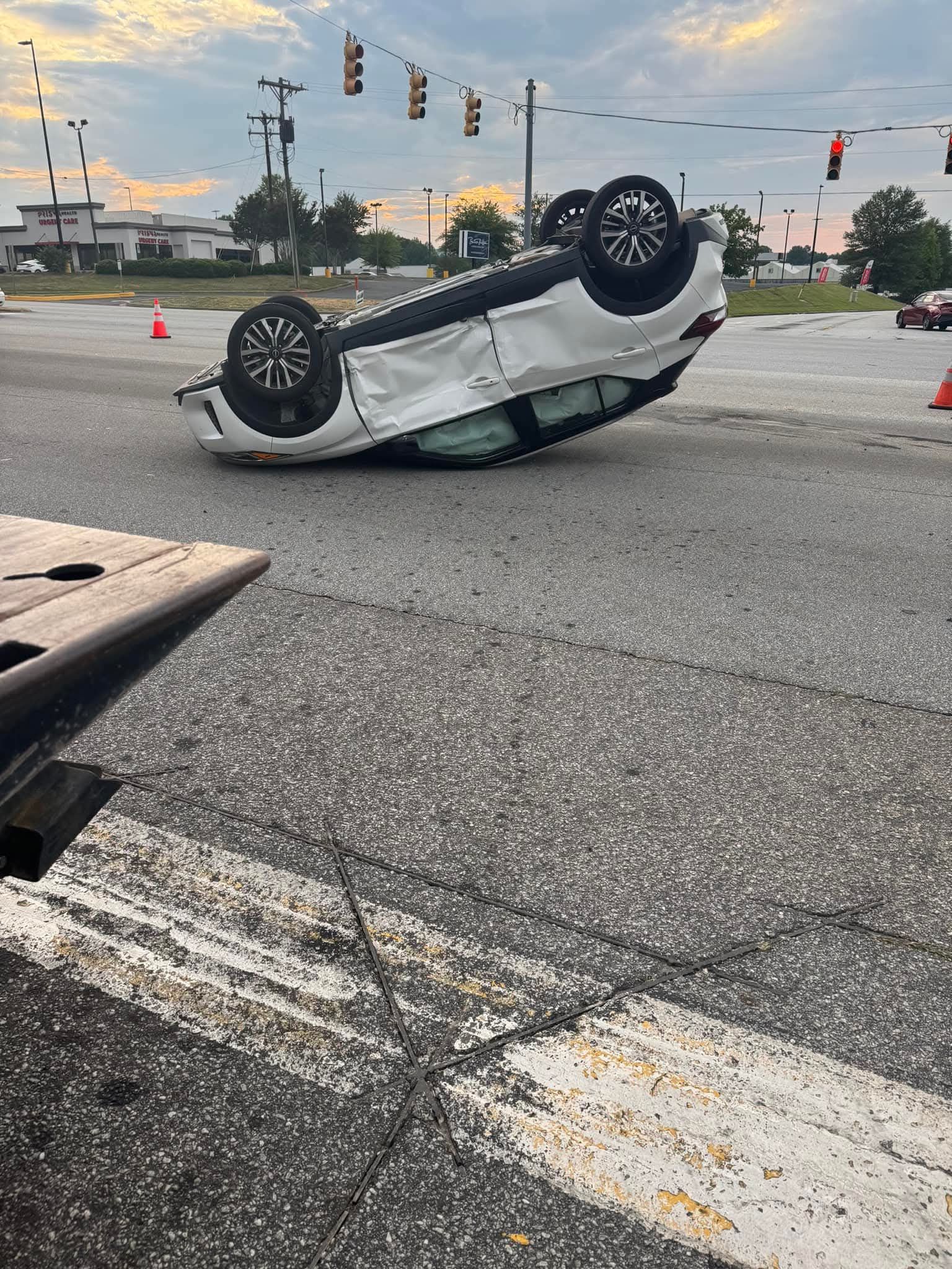 A white car flipped over in the middle of a street at an intersection.
