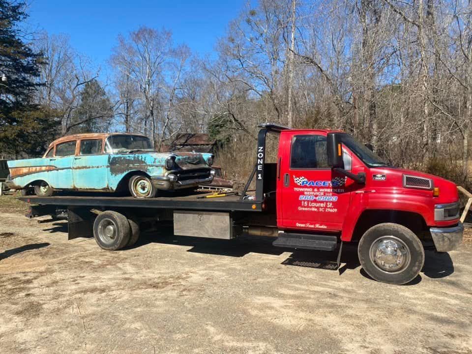 Red tow truck transporting a weathered blue classic car on a sunny day.