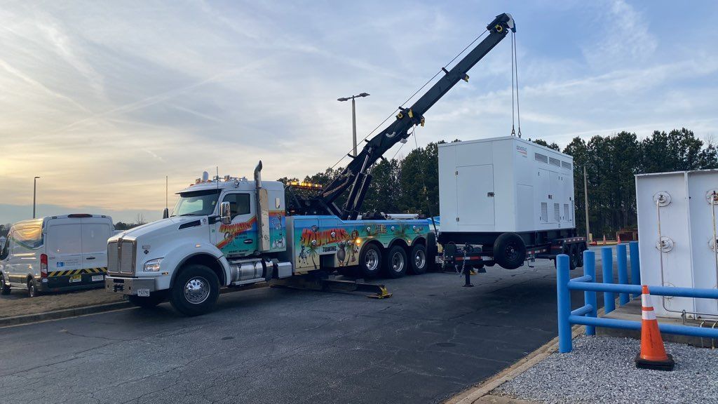 Tow truck lifting a white container on a flatbed truck in a parking lot at sunset