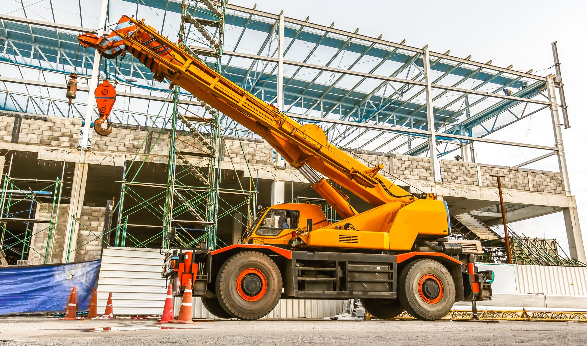 Yellow mobile crane at a construction site, lifting materials near a building frame.