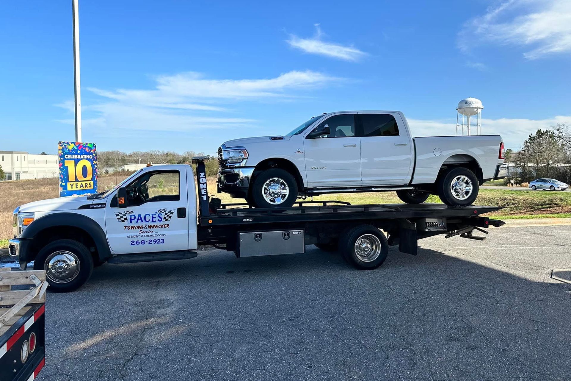White tow truck carrying a white pickup truck on a sunny day.