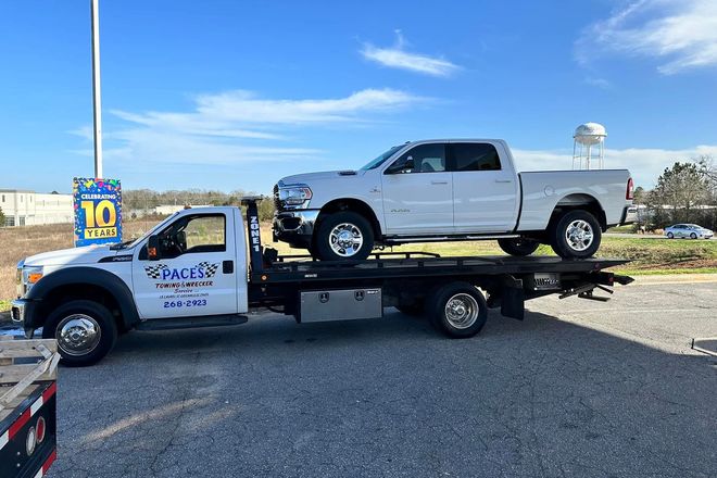 White tow truck carrying a white pickup truck on a sunny day.