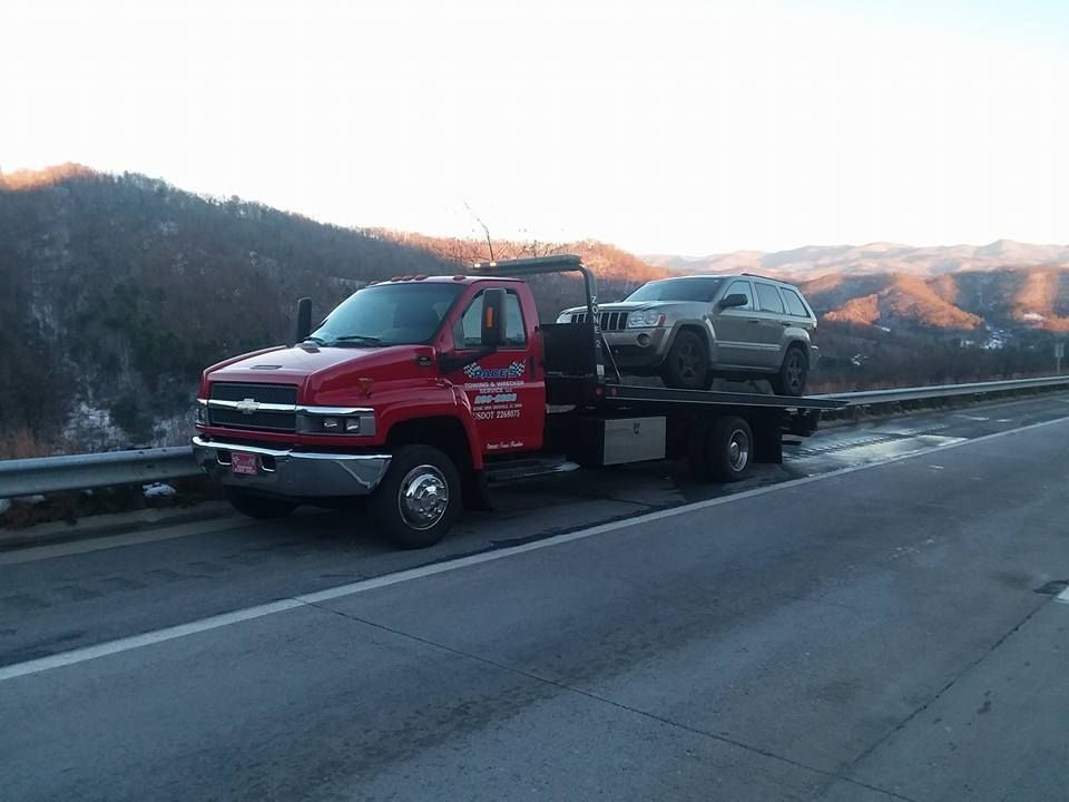 Red tow truck carrying a gray SUV on a highway, mountains in the background.