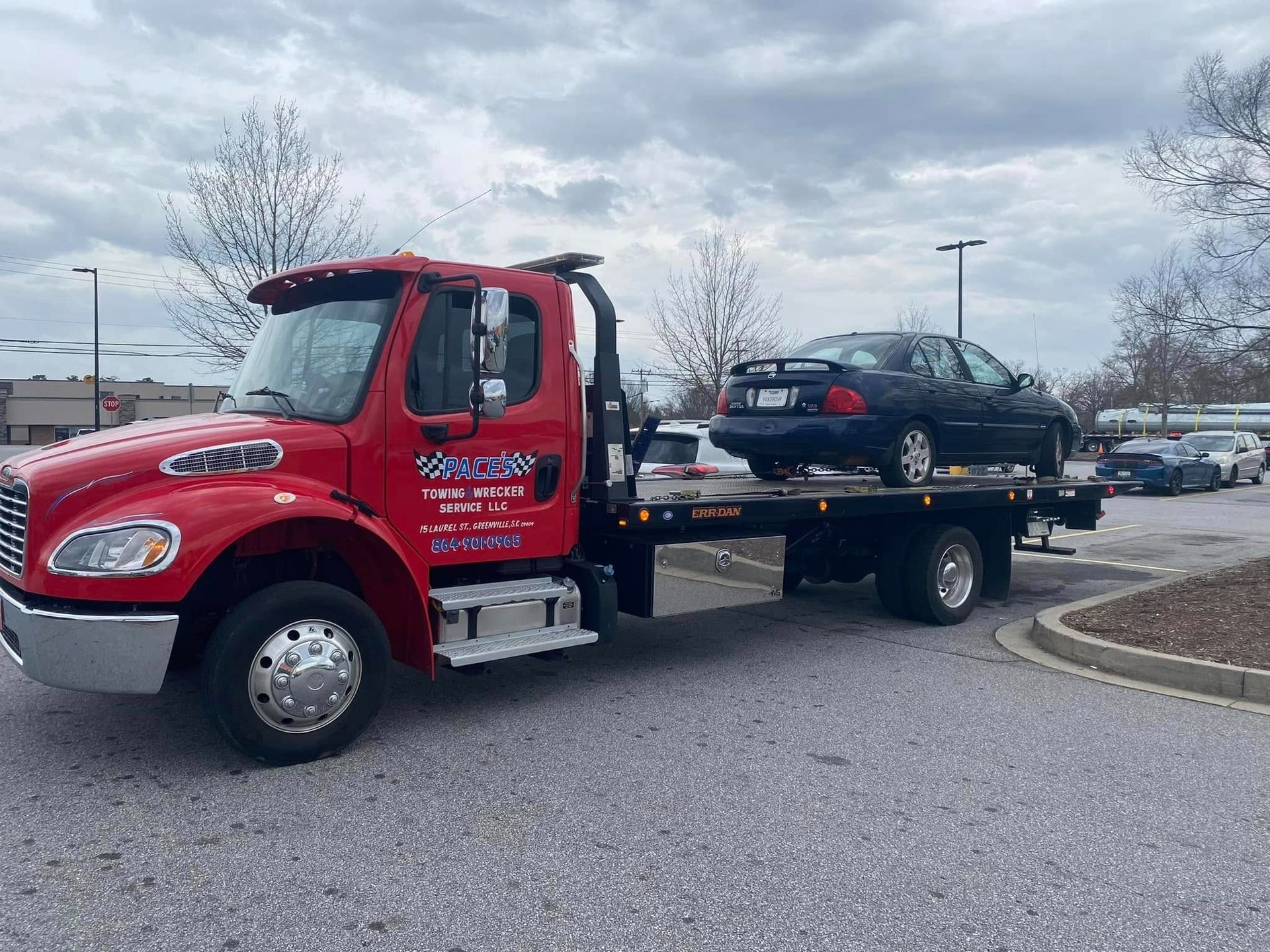 Red tow truck transporting a gray SUV on a highway, mountains in the background.