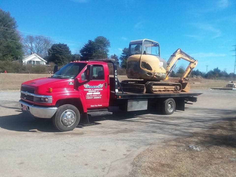 Red flatbed truck carrying a yellow mini excavator outdoors on a sunny day.