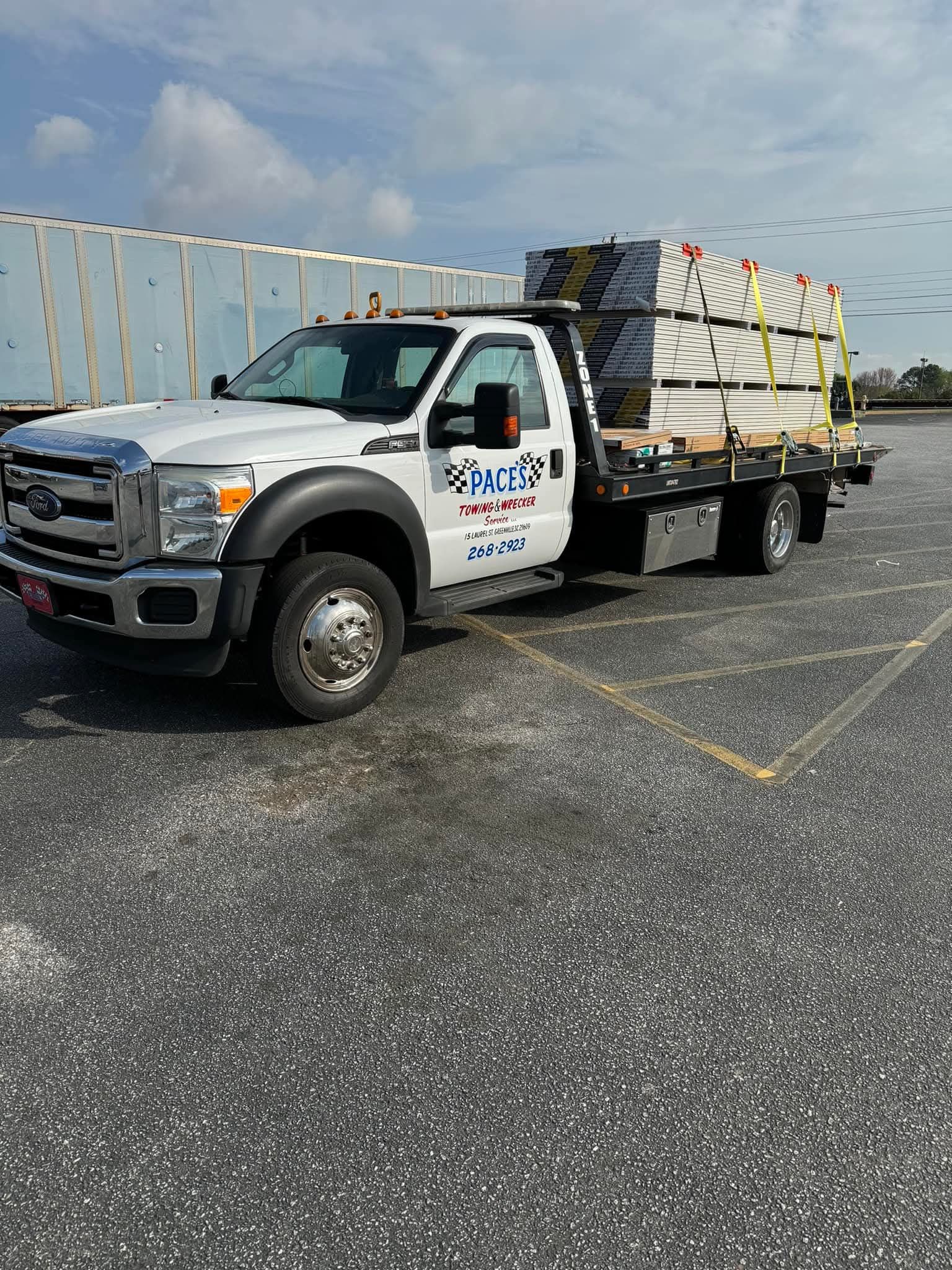 White Ford truck carrying lumber on a blacktop parking lot.