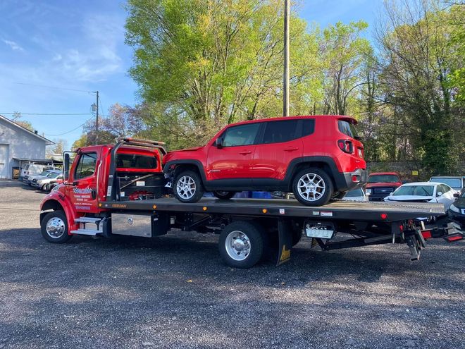 Red SUV on a red tow truck at a lot. Sunny day.