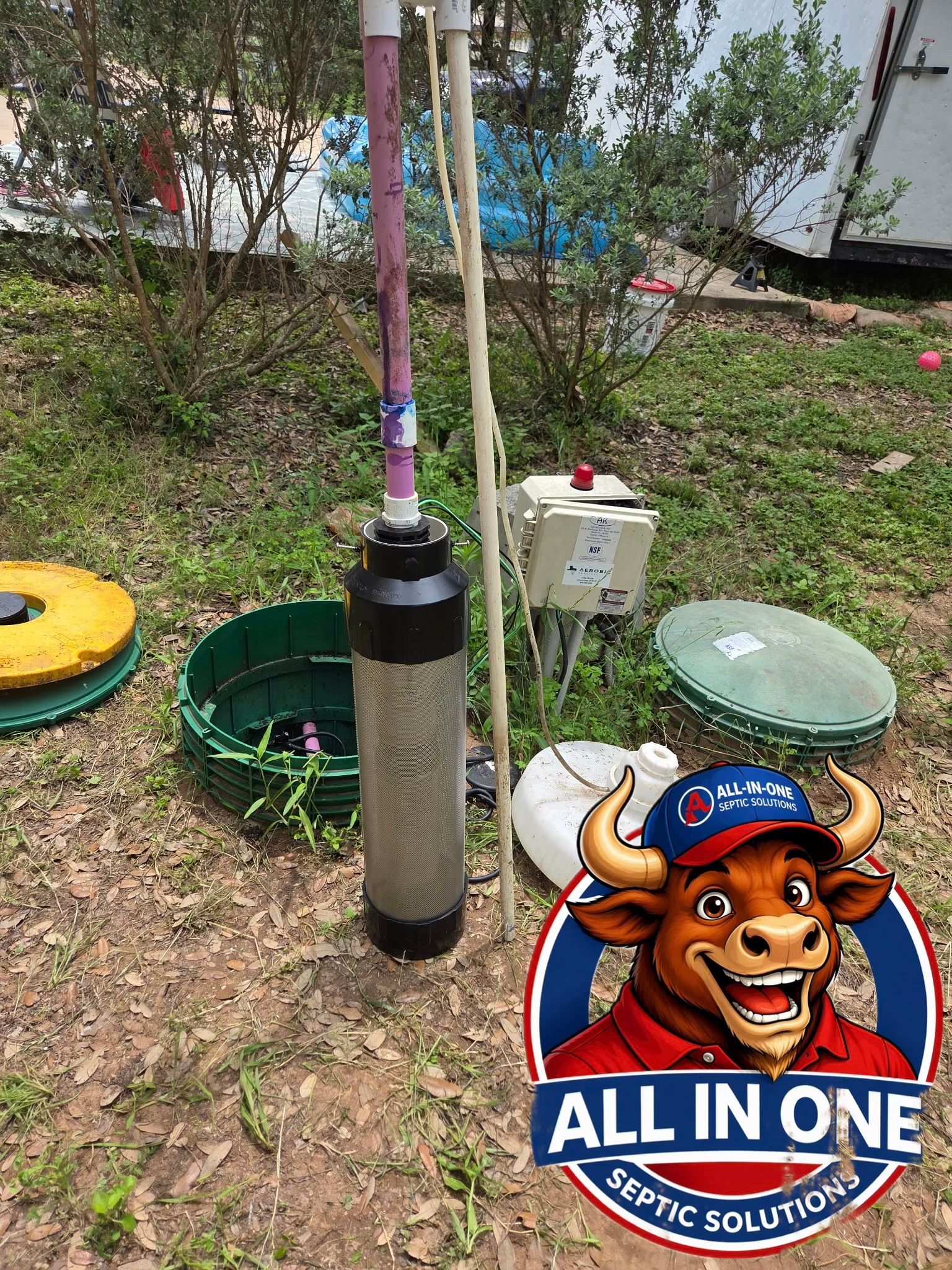 Metal cylinder with purple hose standing in a grassy yard, next to a small box and round plastic lids.