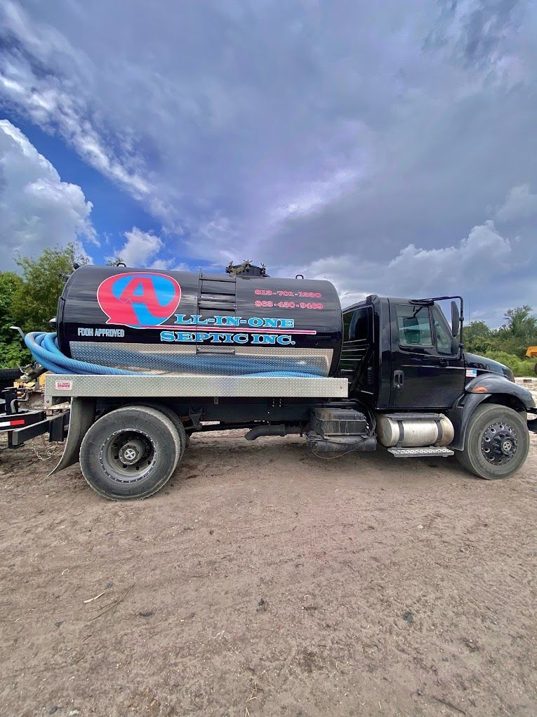 A black septic tank truck is parked in a dirt lot.