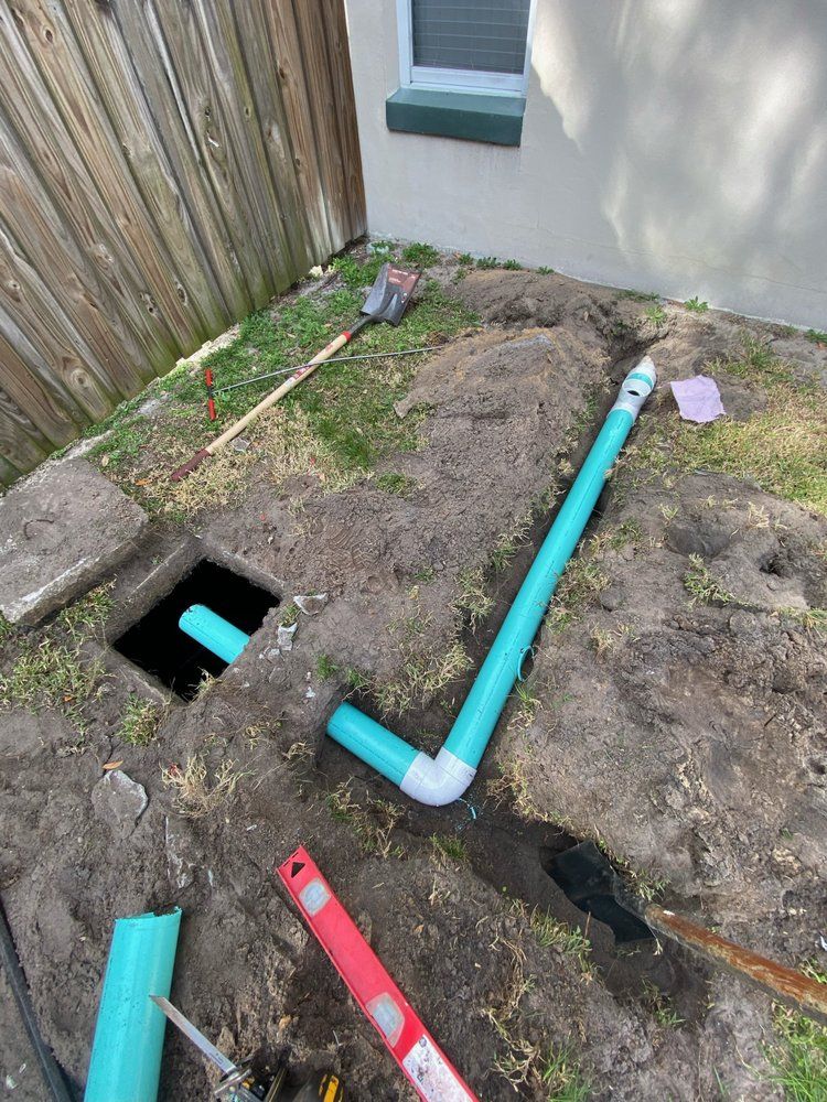 A green pipe is laying in the dirt next to a hole in the ground.