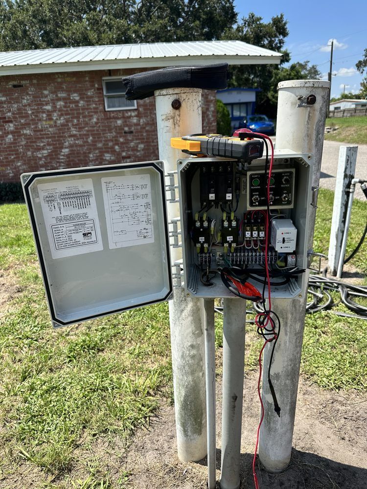 A electrical box is sitting on top of a pole in a grassy field.
