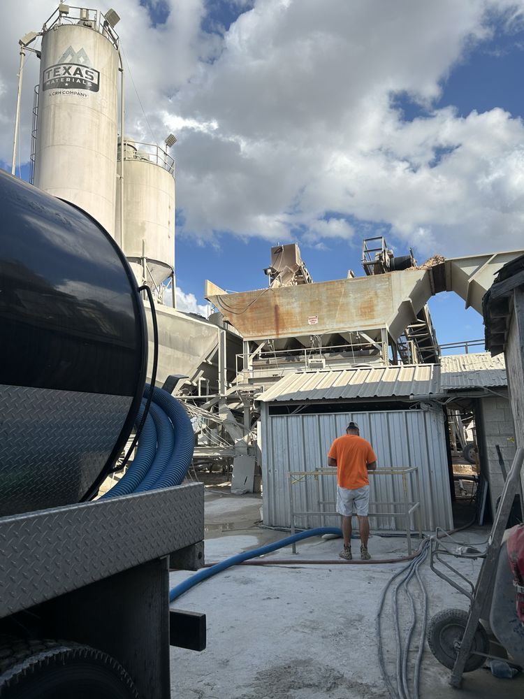 A man in an orange shirt is standing in front of a concrete plant.