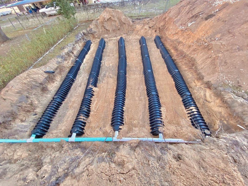 A row of black pipes are sitting in the dirt.