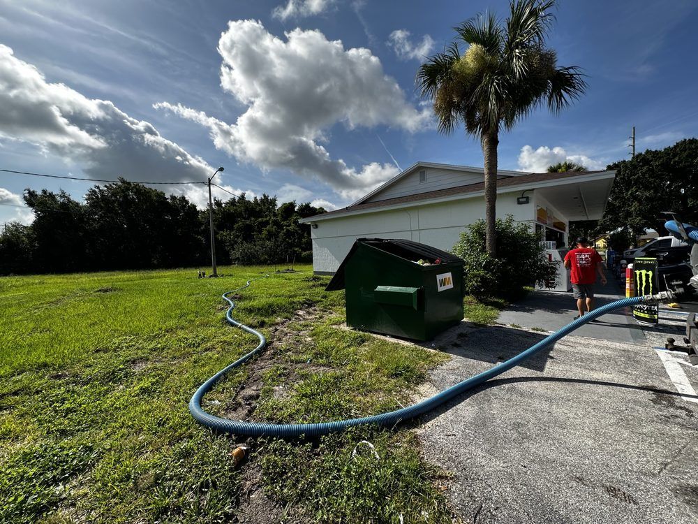 A hose is connected to a green dumpster in front of a house.
