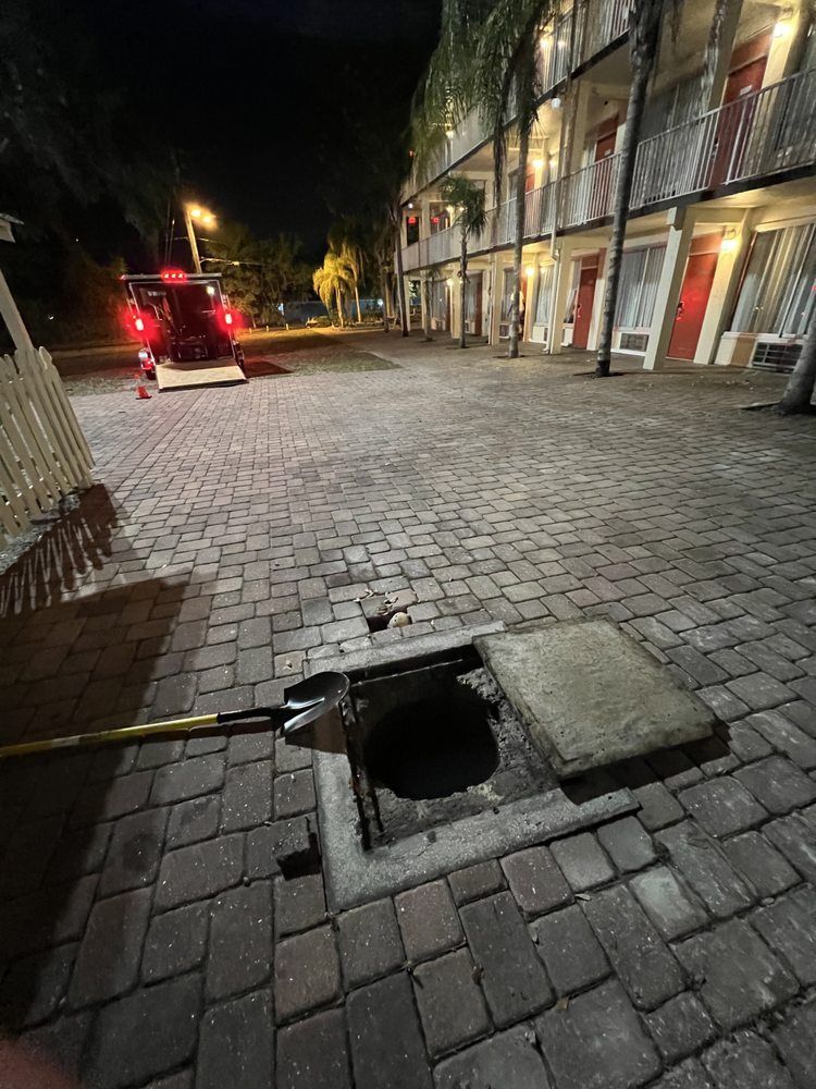 A manhole cover is open in front of a building at night.