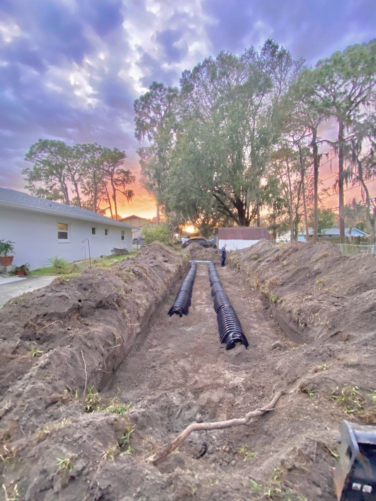 A drainage system is being installed in the dirt in front of a house.