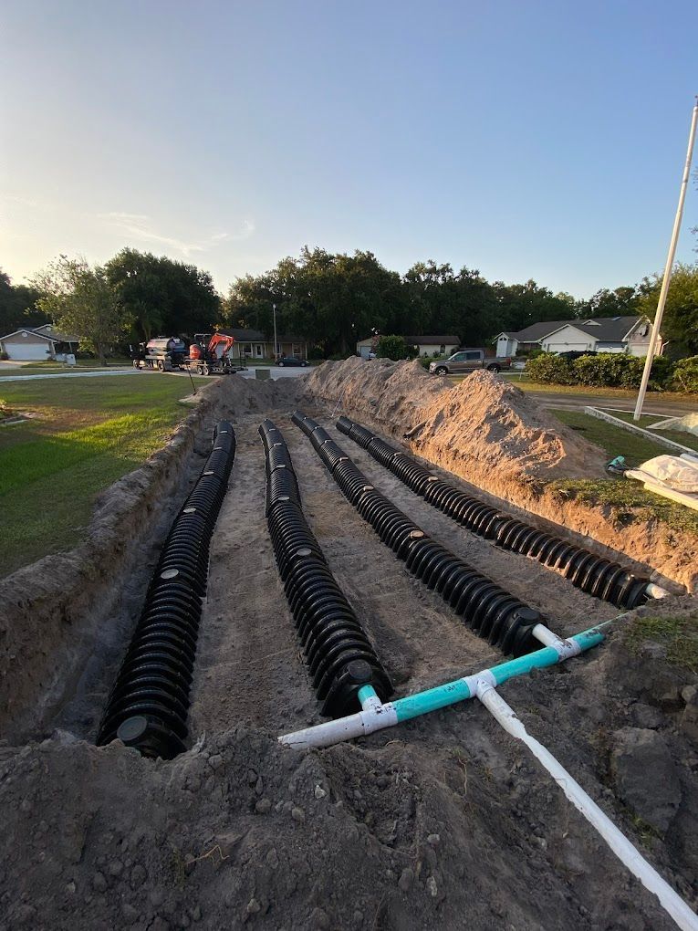 A row of septic tanks are being installed in a dirt field.