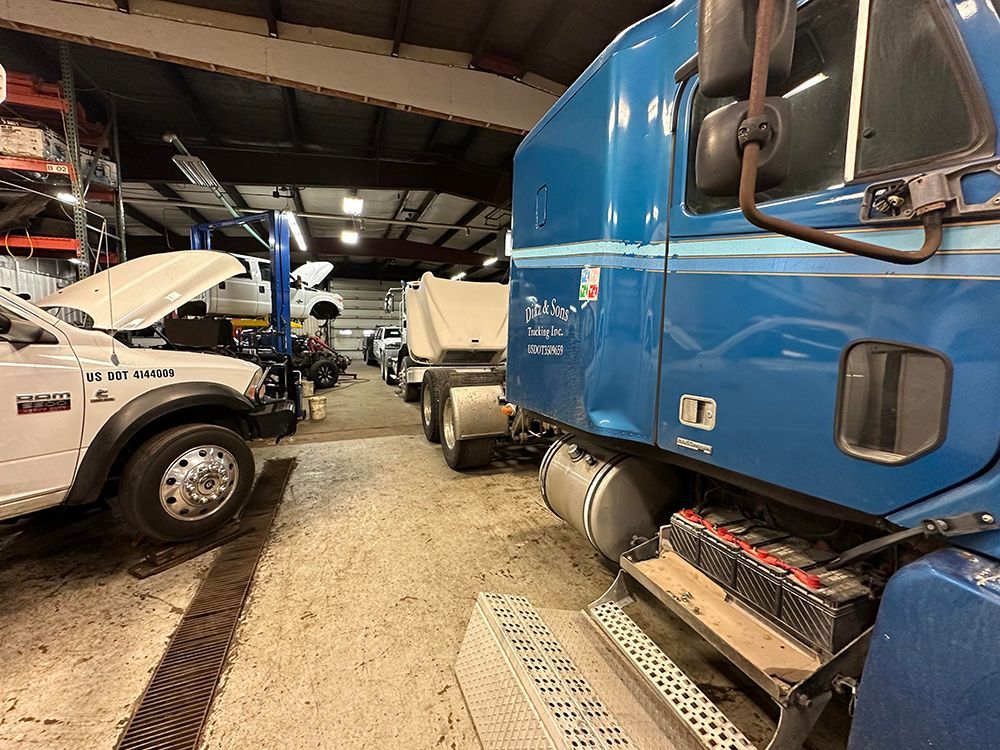 A blue truck is parked in a garage next to a white truck