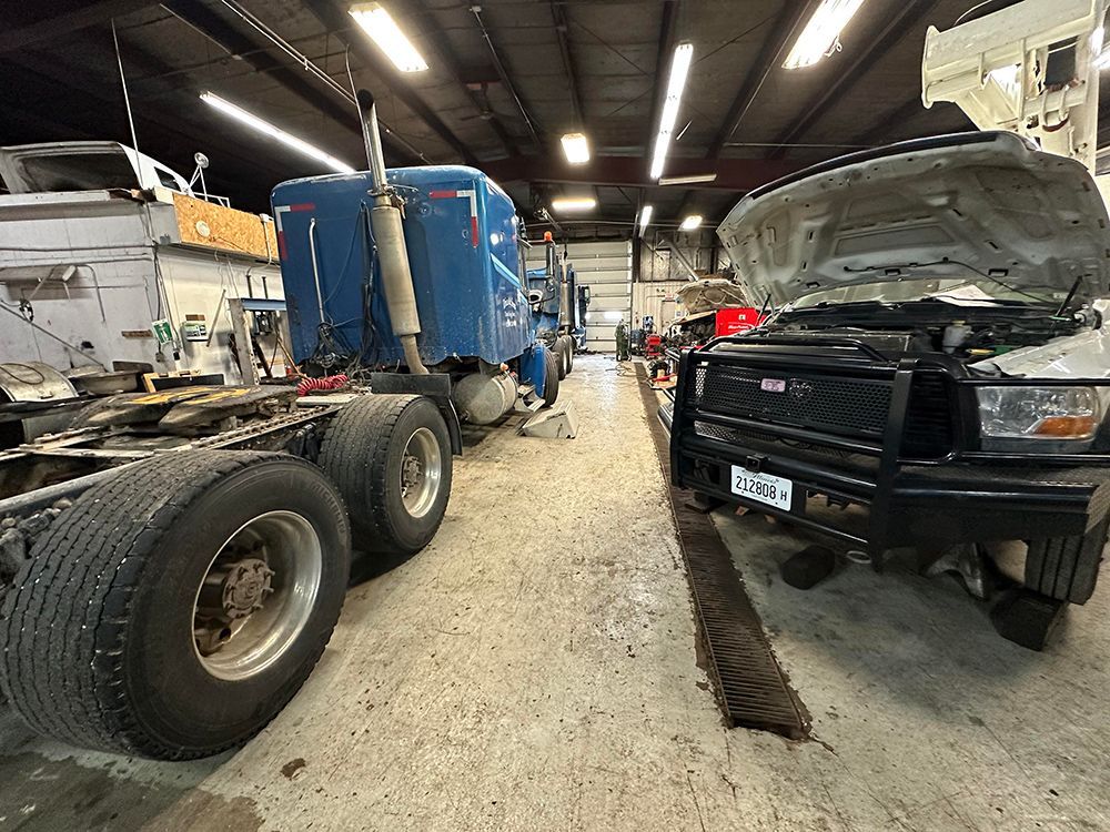 A truck and a truck with the hood open are in a garage.