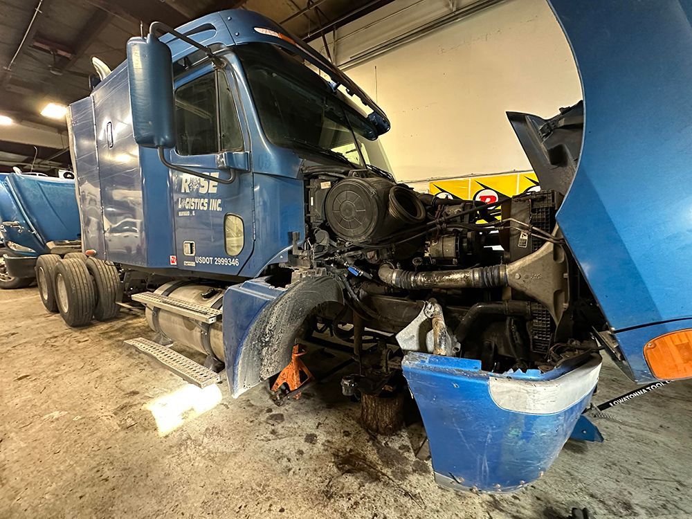 A blue semi truck with its hood open is sitting in a garage