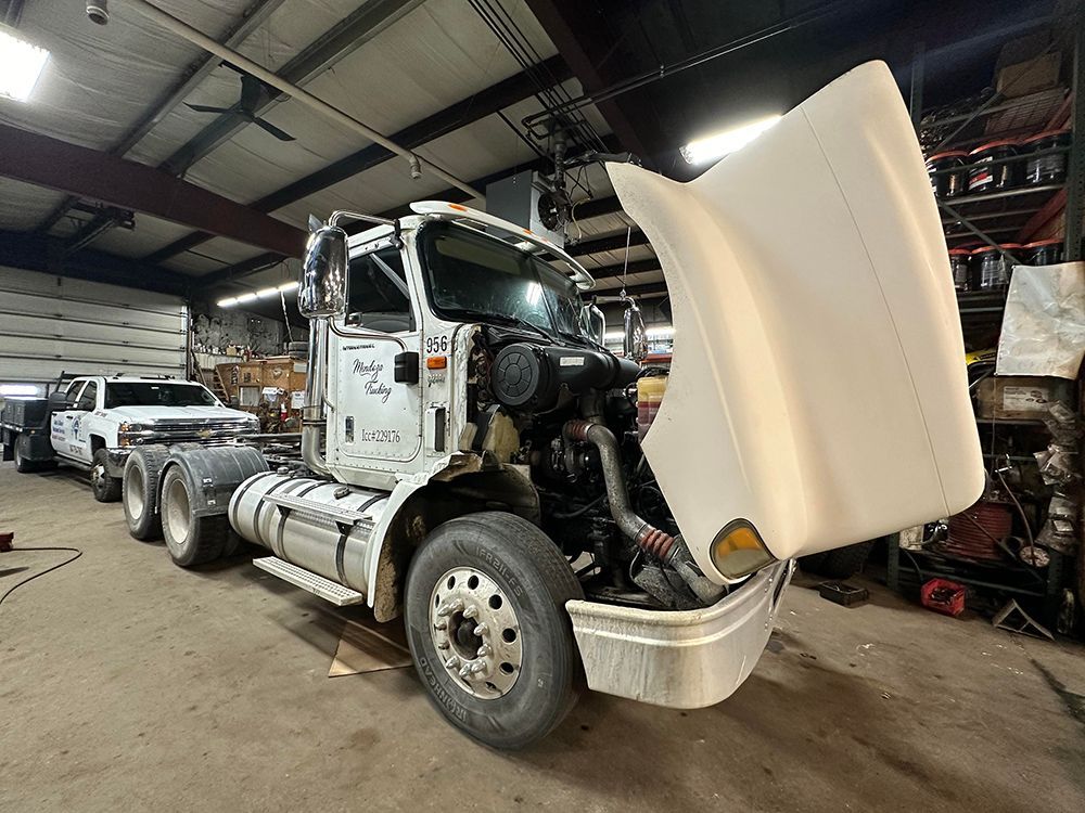 A semi truck with its hood up in a garage