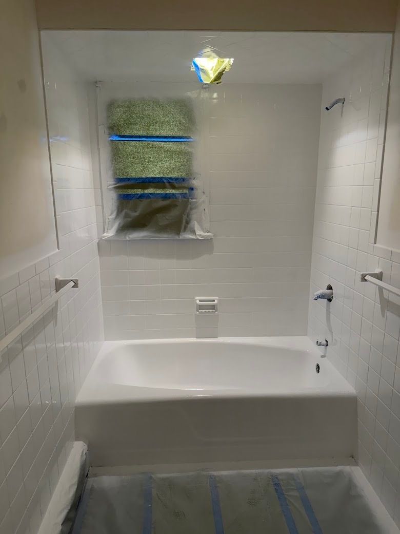 Small white tiled bathroom with bathtub, window covered by a towel, and a ceiling light fixture.