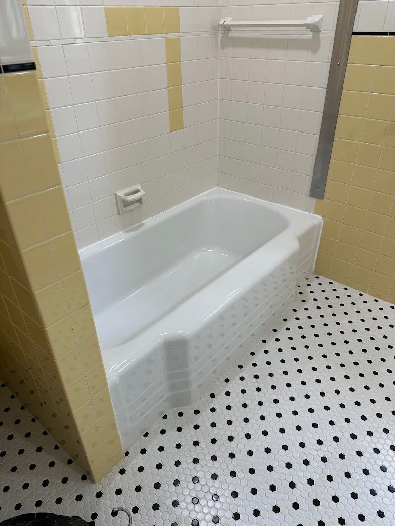 Compact bathtub in a tiled bathroom with black-and-white mosaic floor.