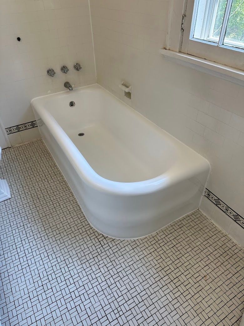 White clawfoot bathtub in a tiled bathroom beside a window.