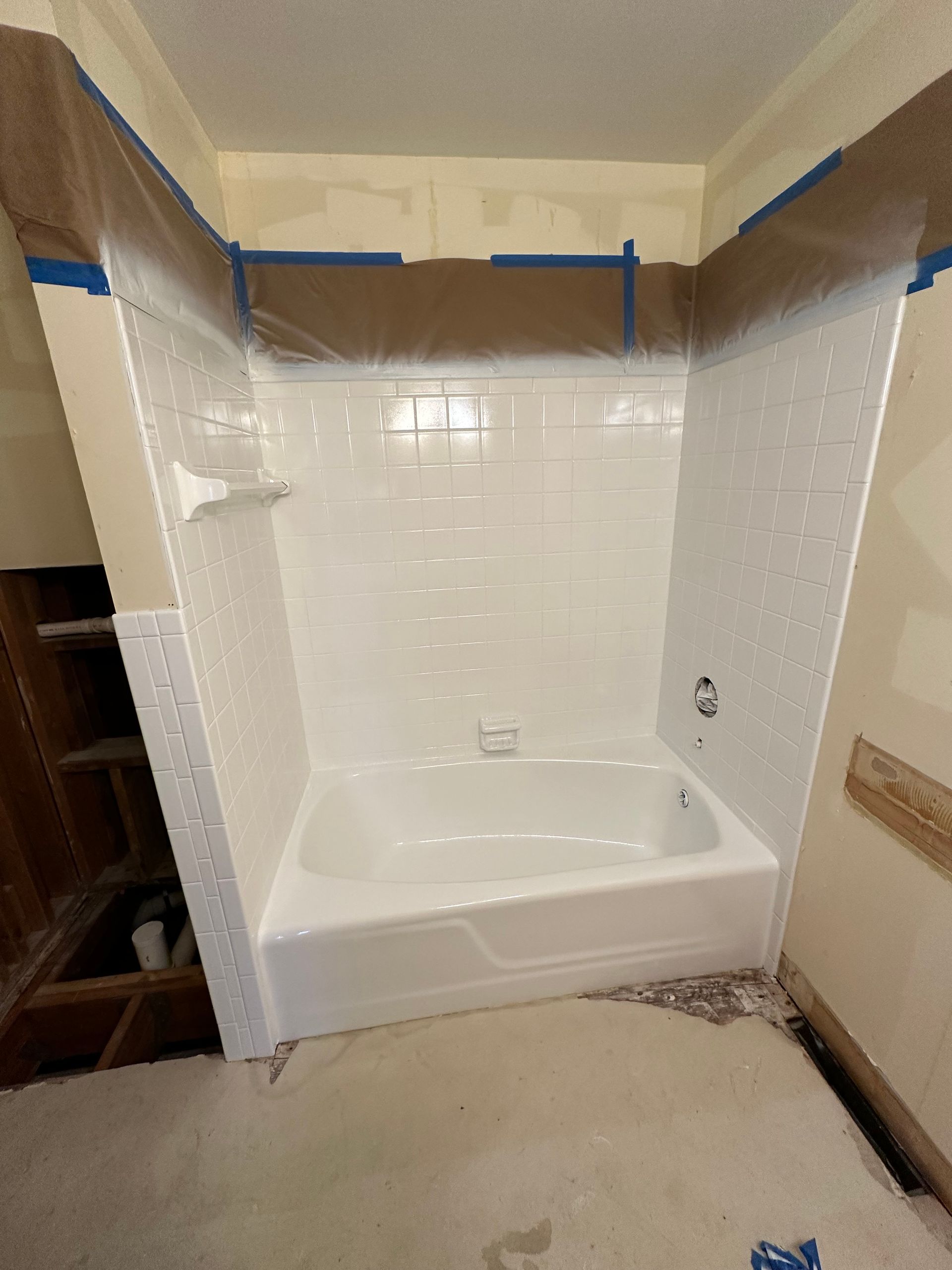 Partially renovated bathtub alcove with white tile, blue painter’s tape, and unfinished surrounding walls
