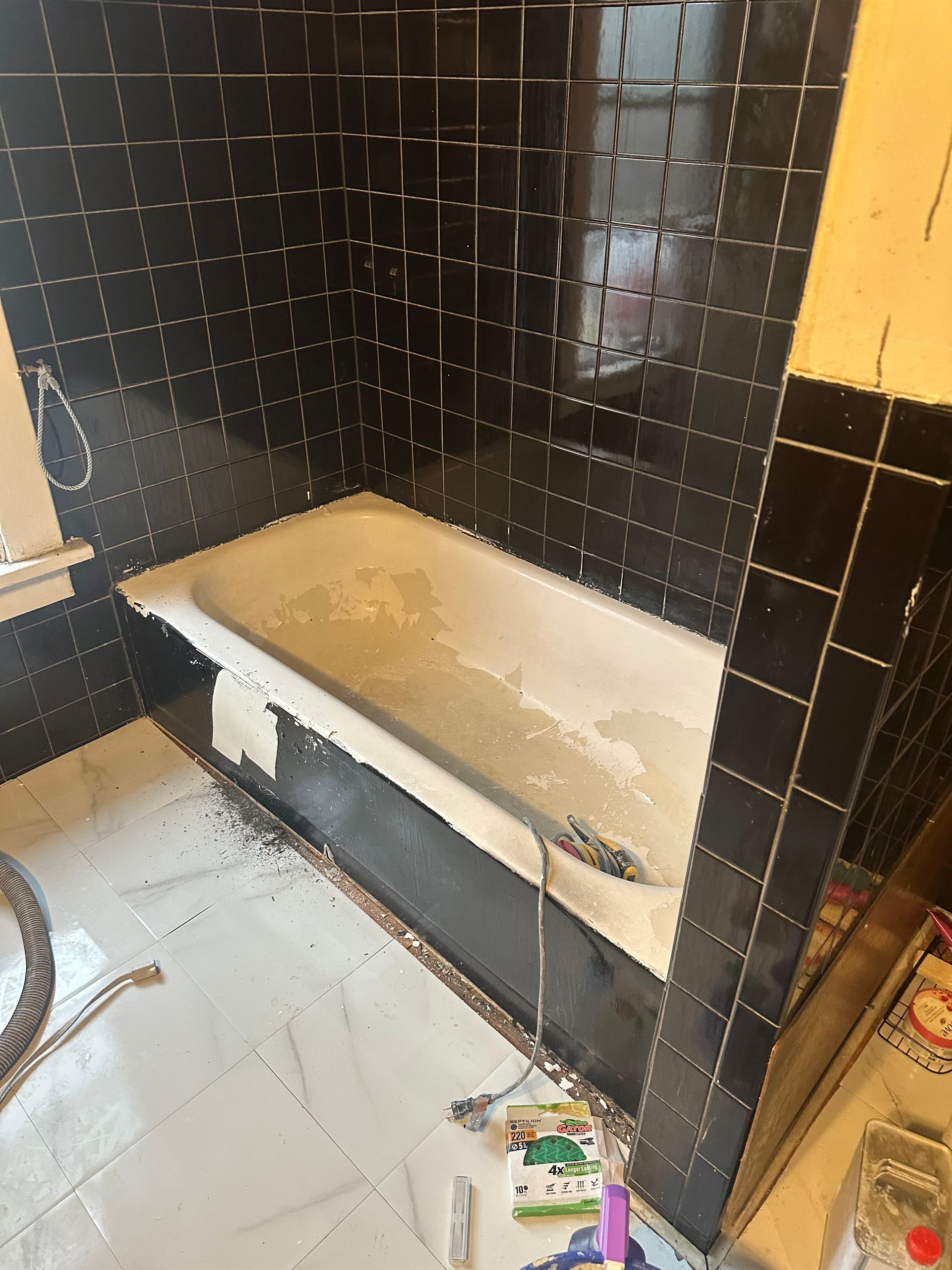 Dirty bathroom with a white bathtub, black tiled walls, and clutter on the floor