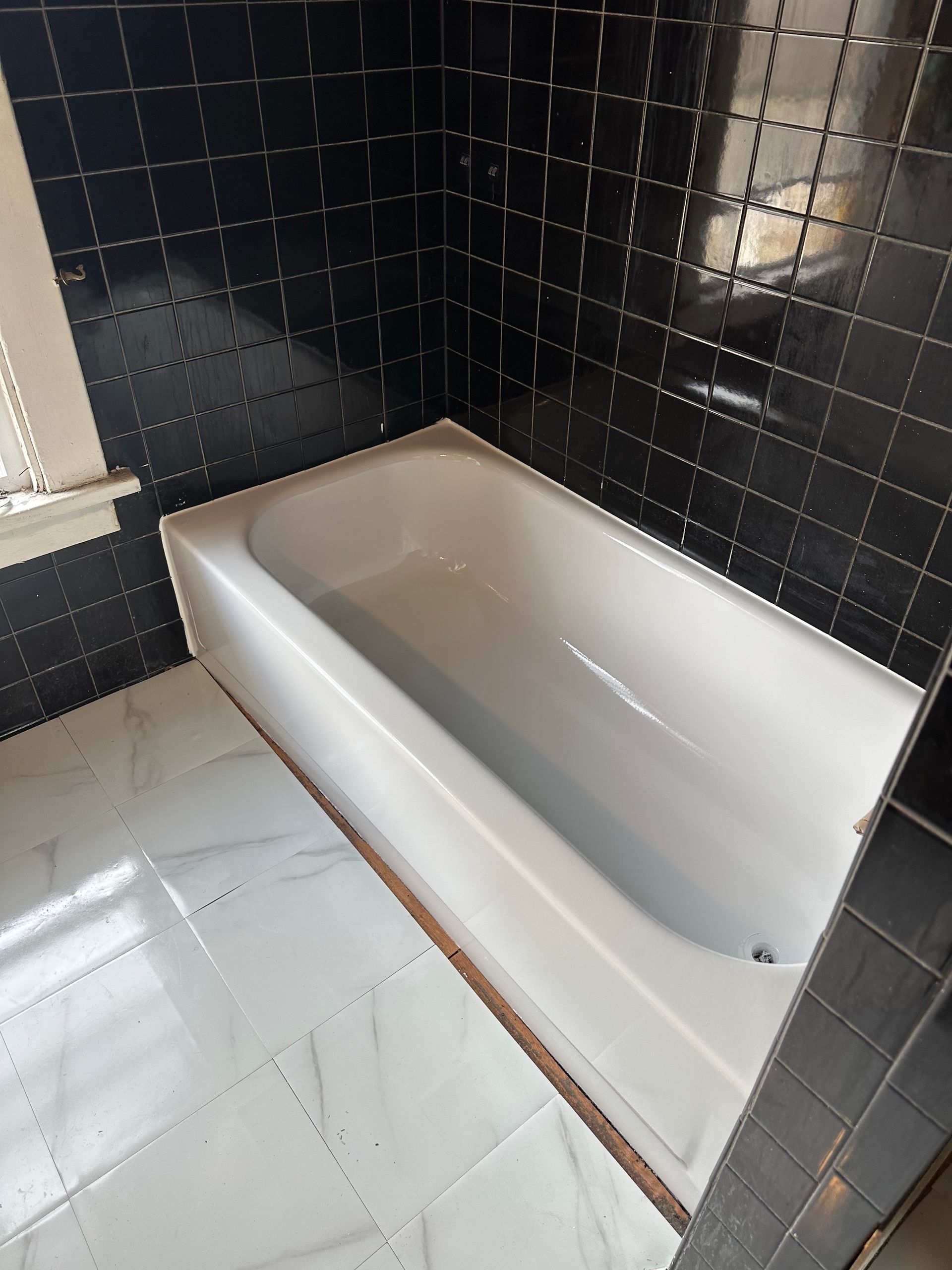 White bathtub in a small bathroom with black tiled walls and white tiled floor.