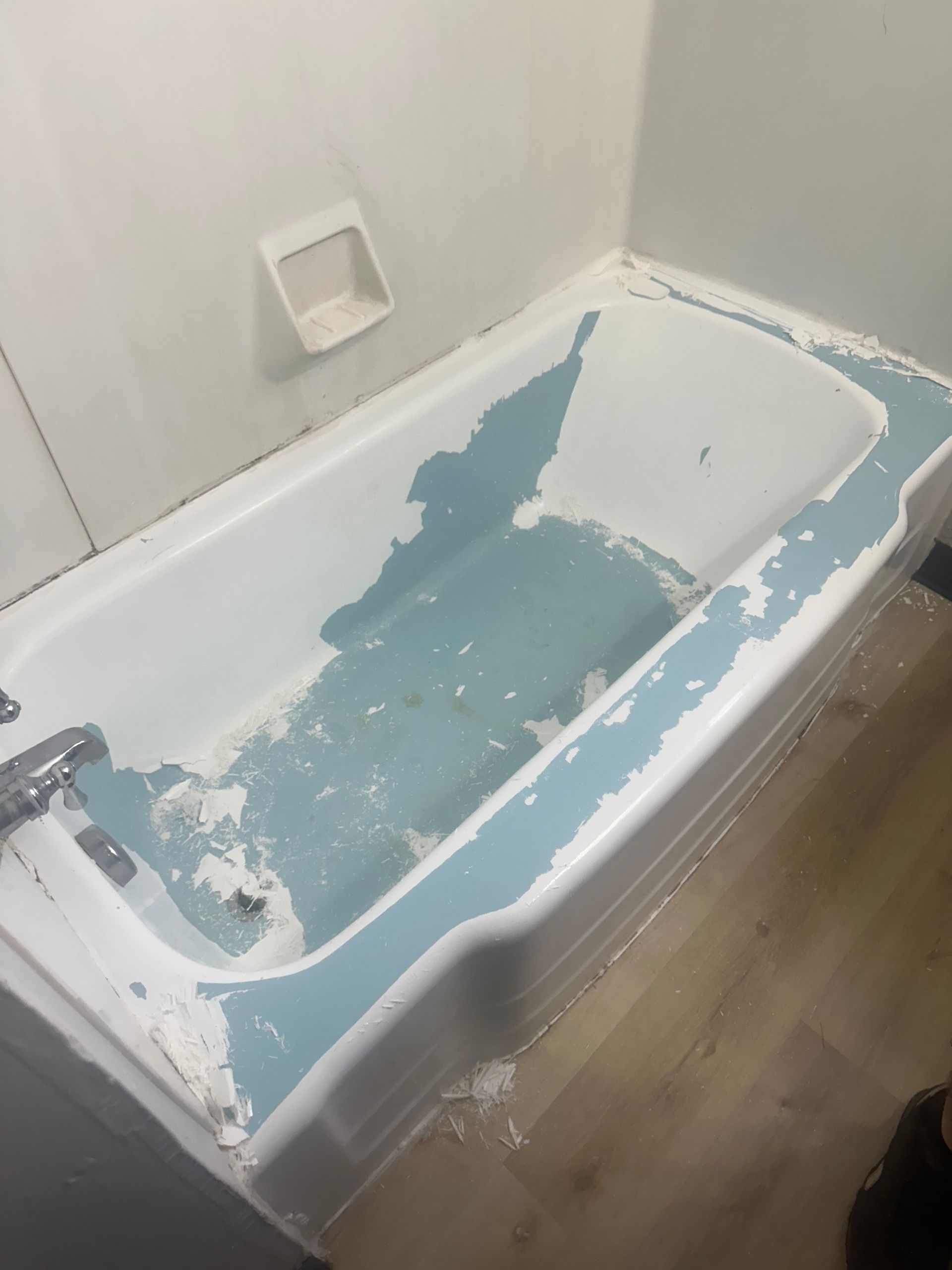 Chipped bathtub with peeling blue paint and white walls in a bathroom