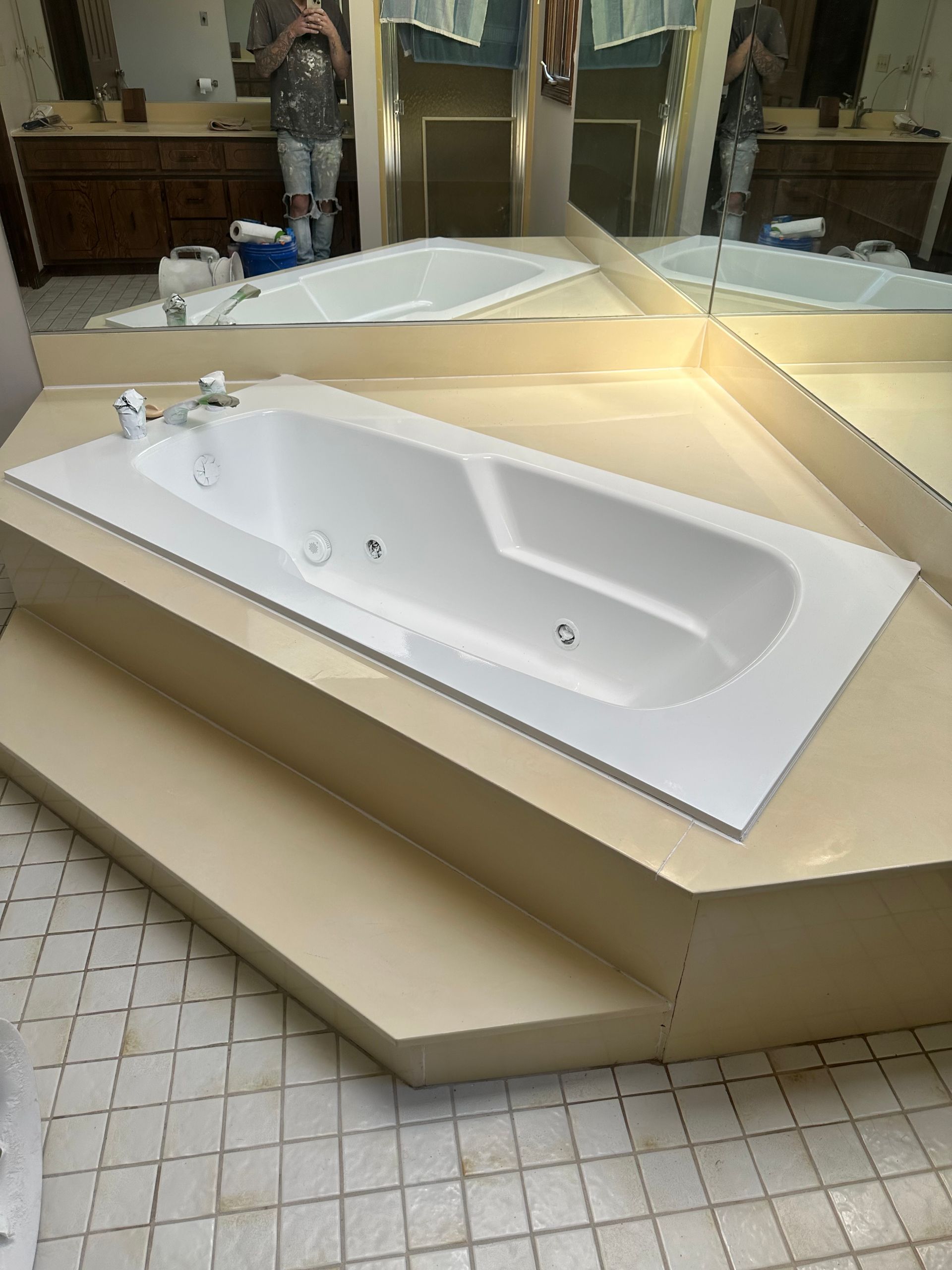 White bathtub in a tiled restroom showroom with beige step platforms and mirrors.