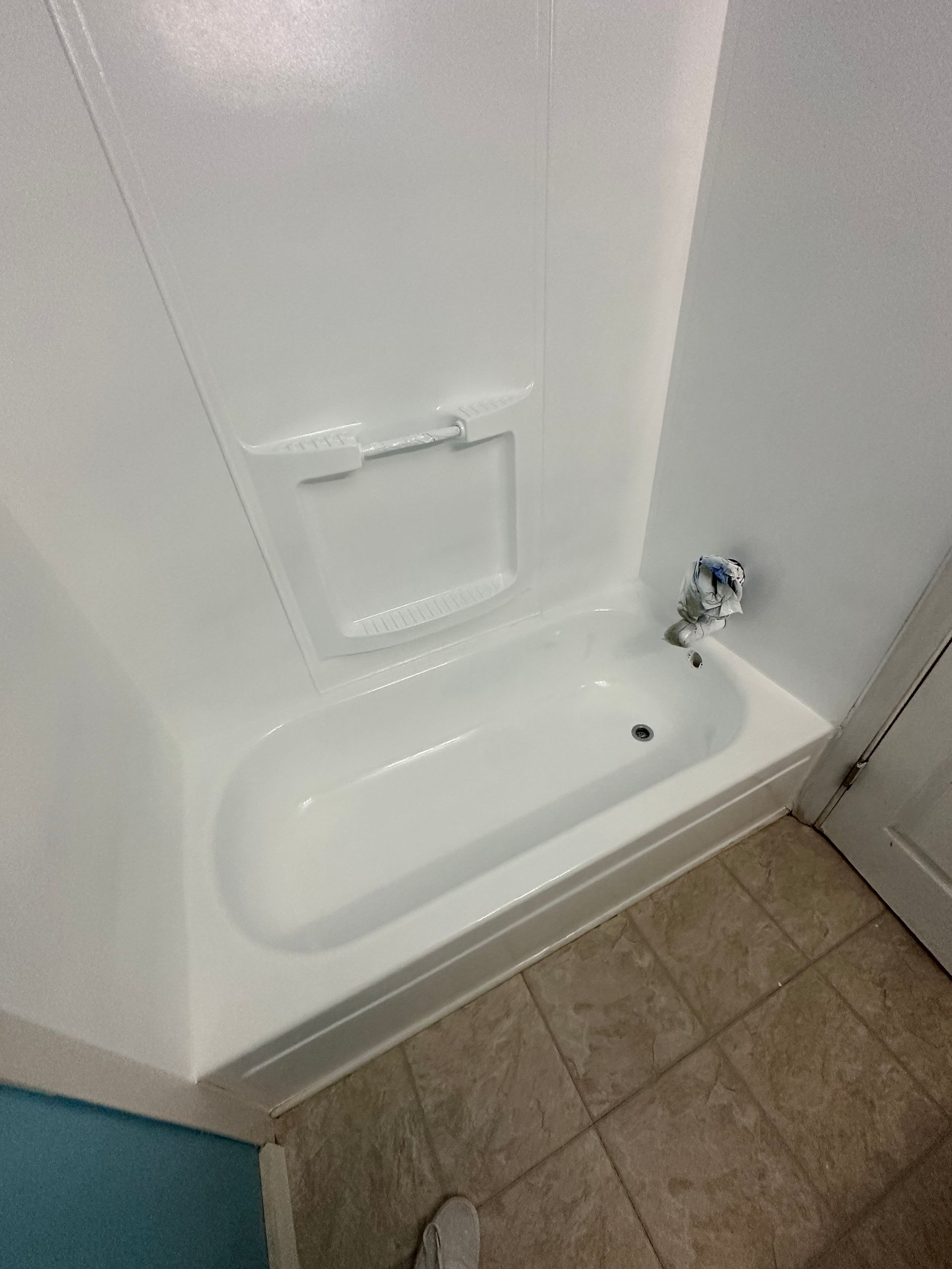 White shower/tub stall with built-in soap dish and chrome showerhead over tan tile floor