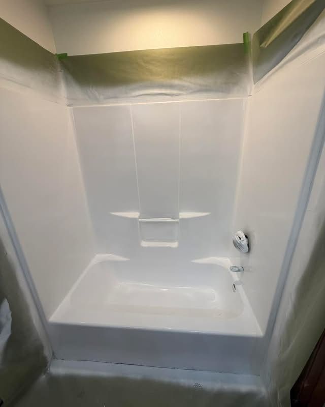 White bathtub and shower surround under renovation, with green painter’s tape along the top edges.
