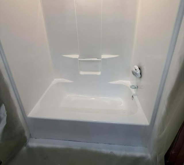 White fiberglass shower stall with built-in shelves and a silver faucet handle on the right side.