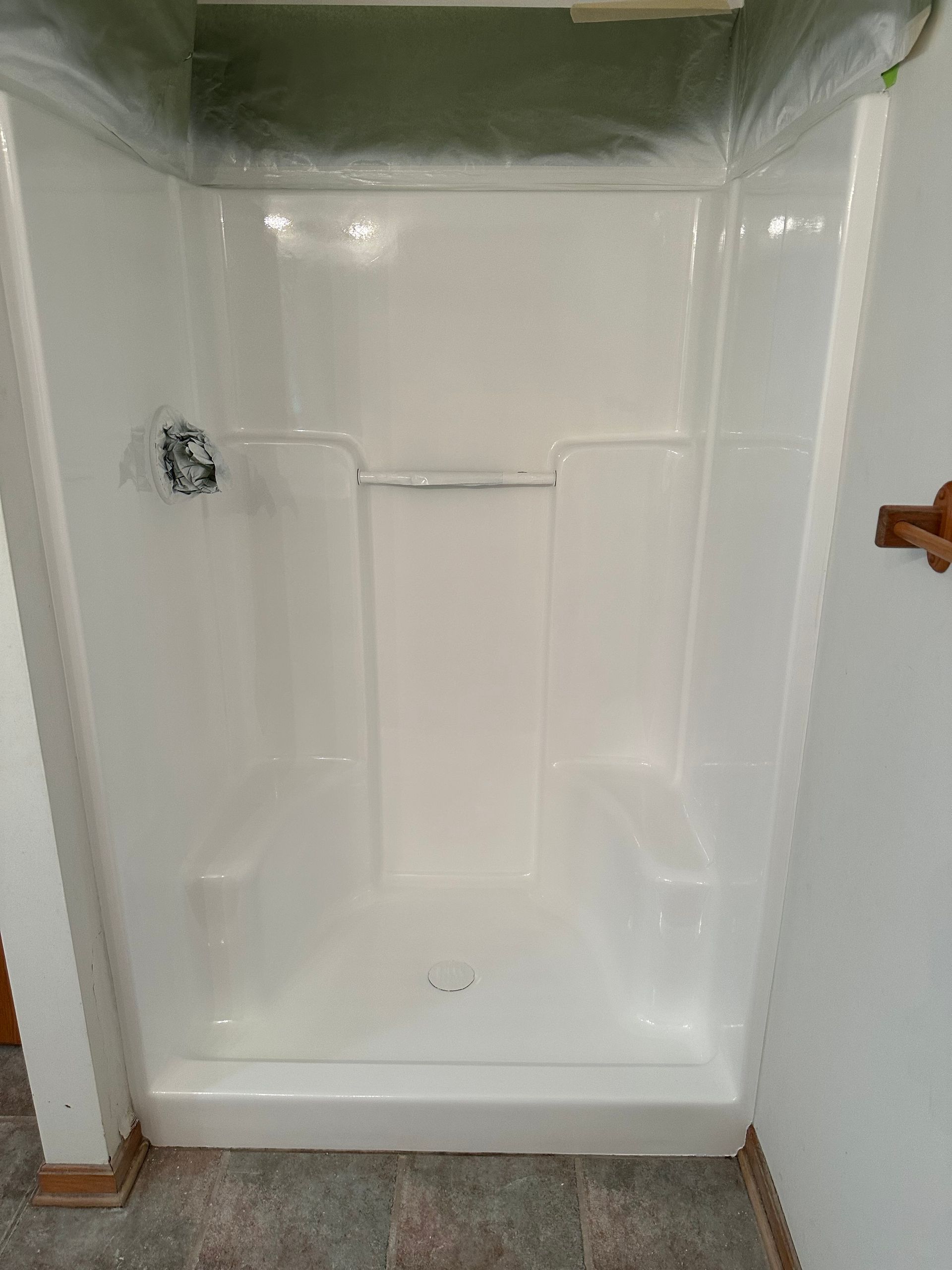 Empty white shower stall with a handheld shower fixture and tan trim