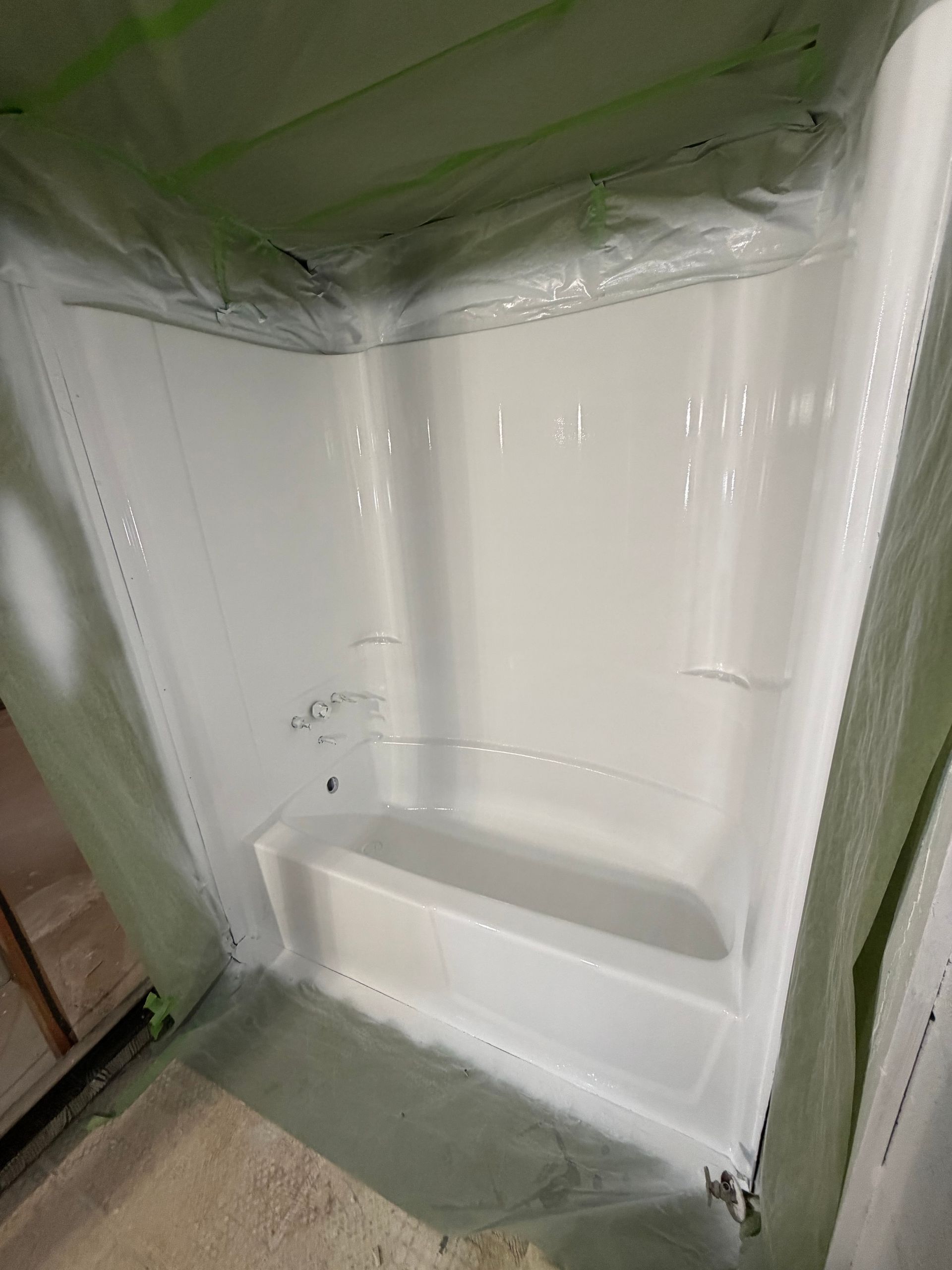 White acrylic shower surround with protective plastic masking and green tape during installation