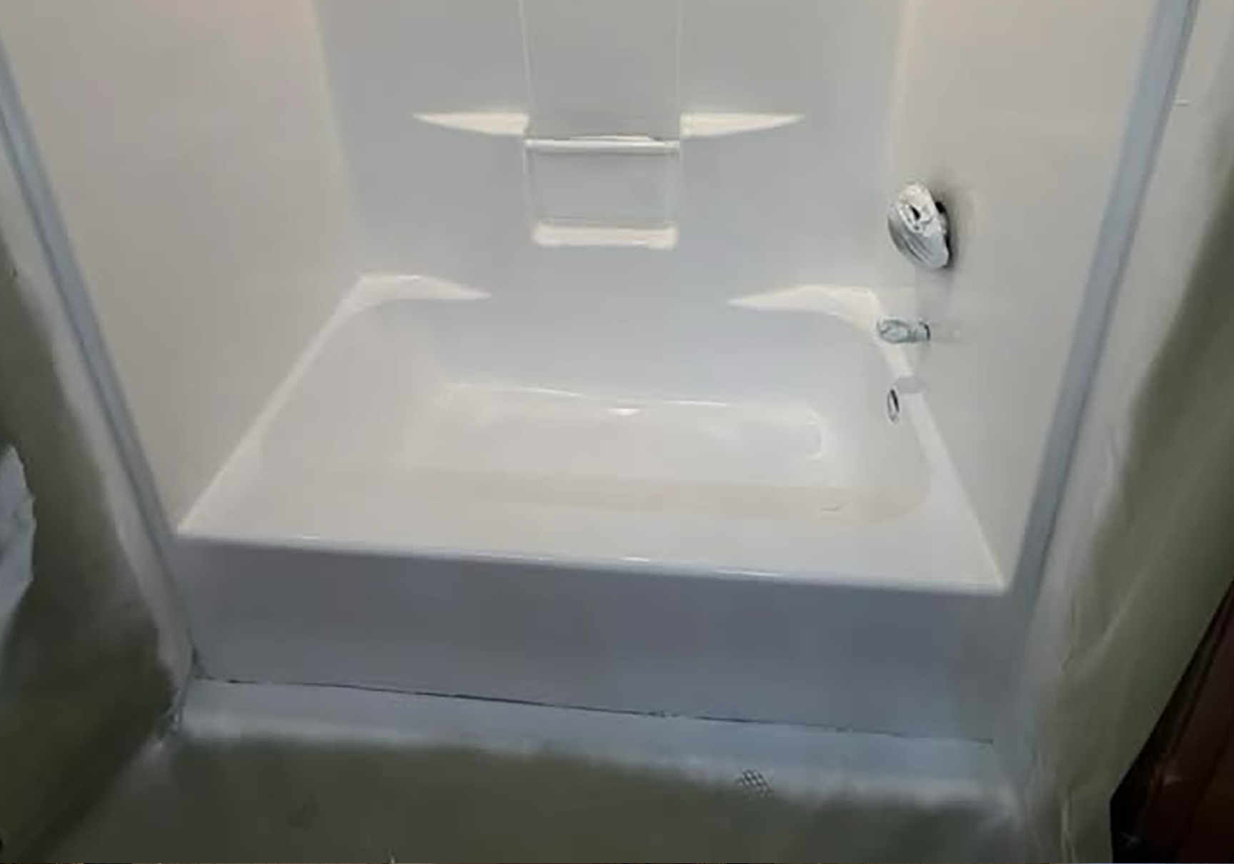 White bathtub/shower with built-in seat and grab bar in a tiled bathroom