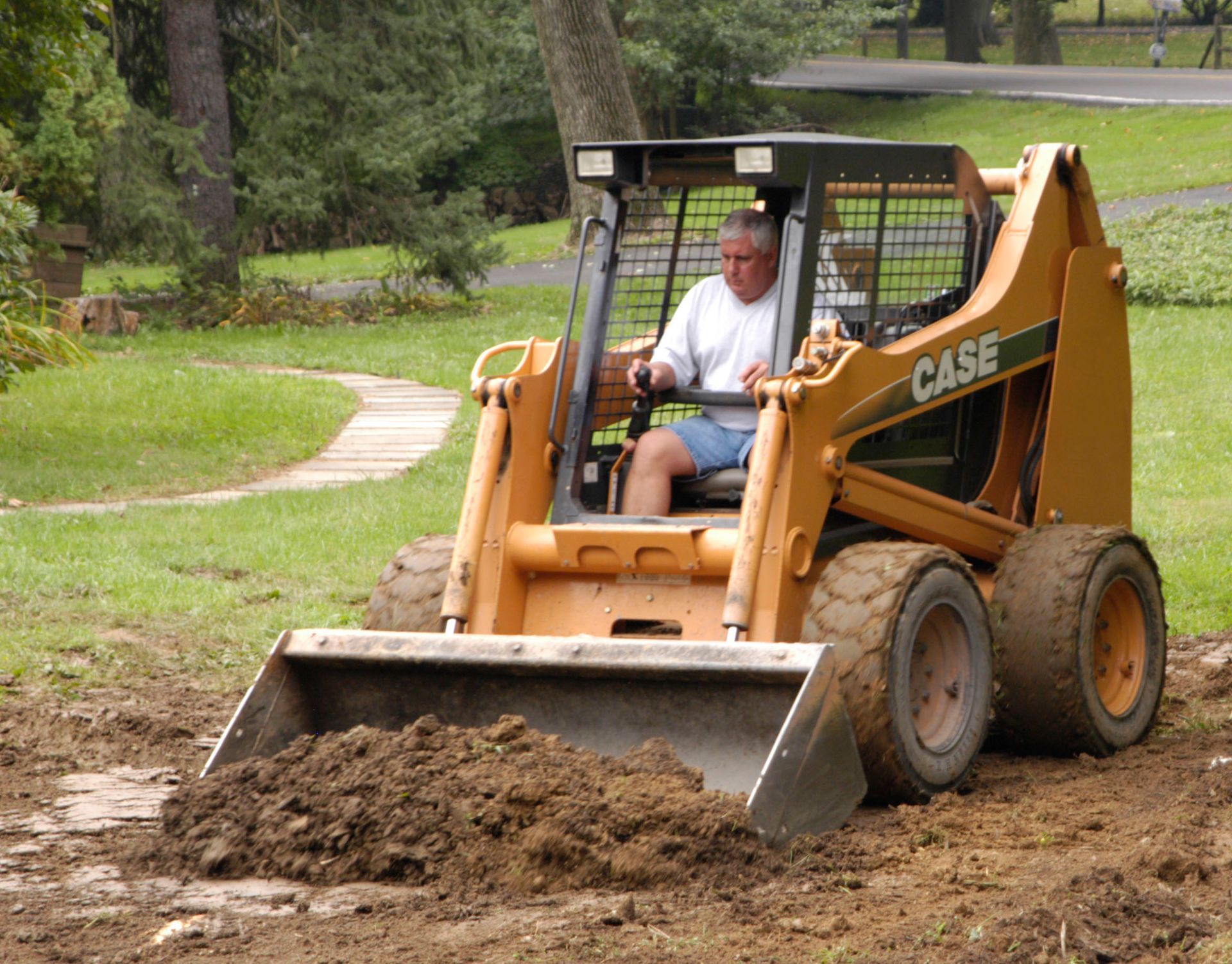 Man operating an orange Case skid steer, moving dirt in an outdoor setting.