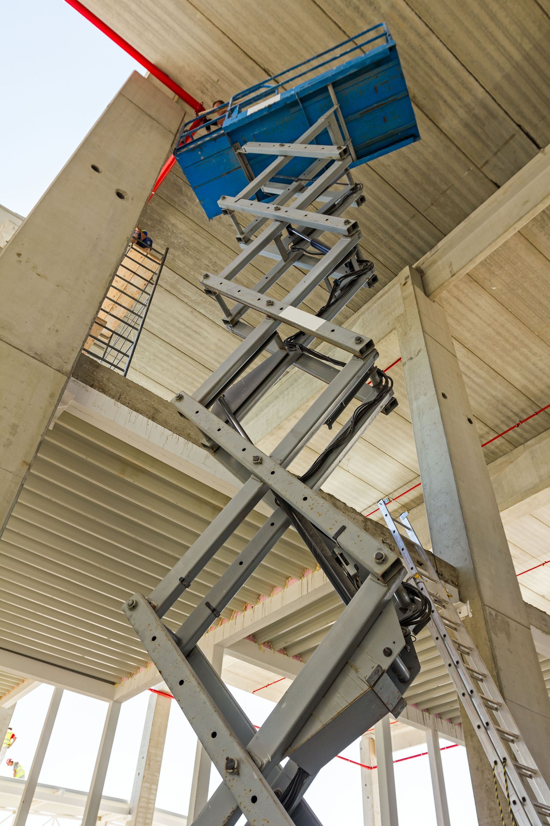 Scissor lift platform raised to ceiling in an unfinished building, with a person working on it.