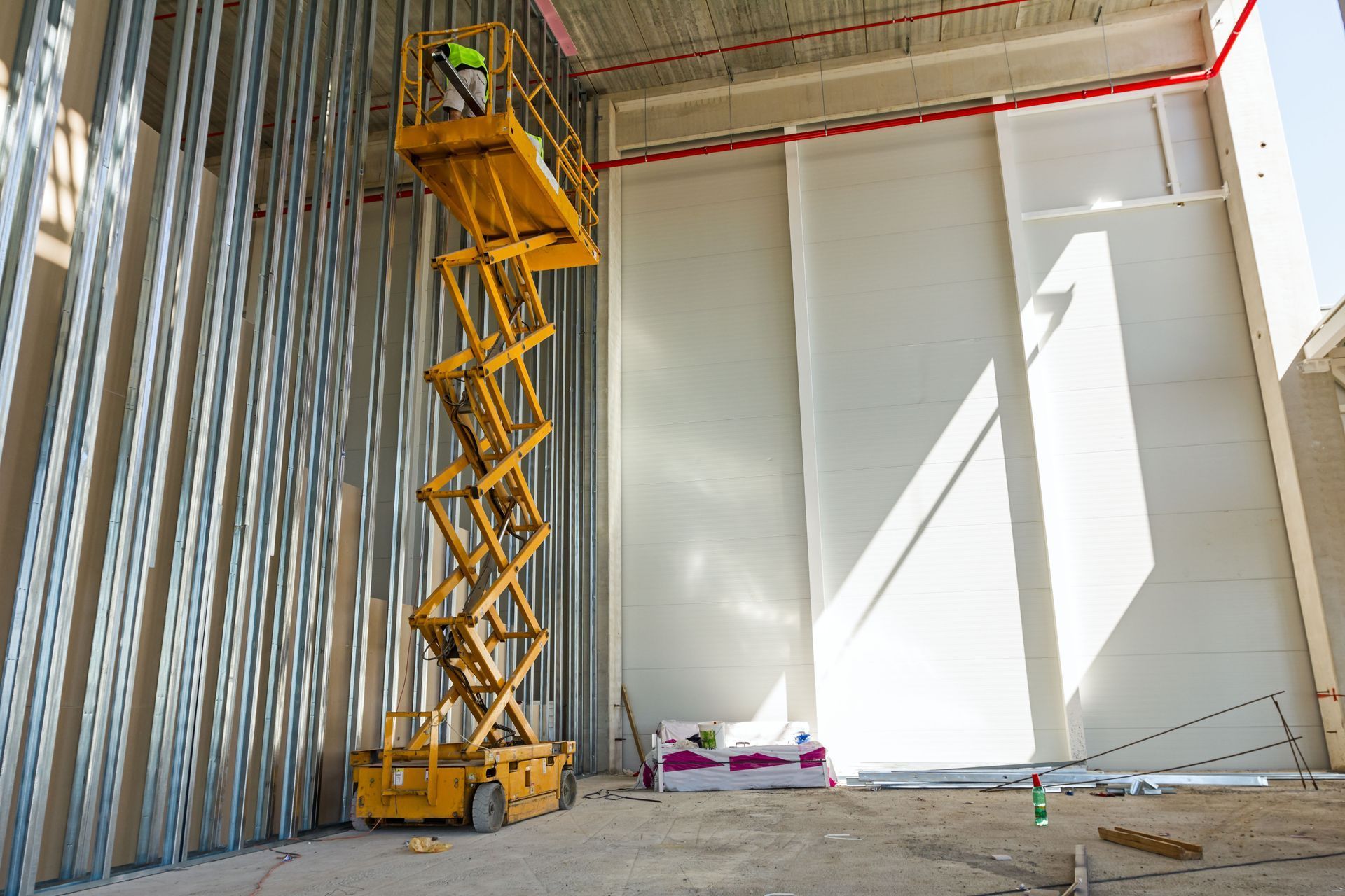 Construction worker on a yellow scissor lift, working inside a building under construction.