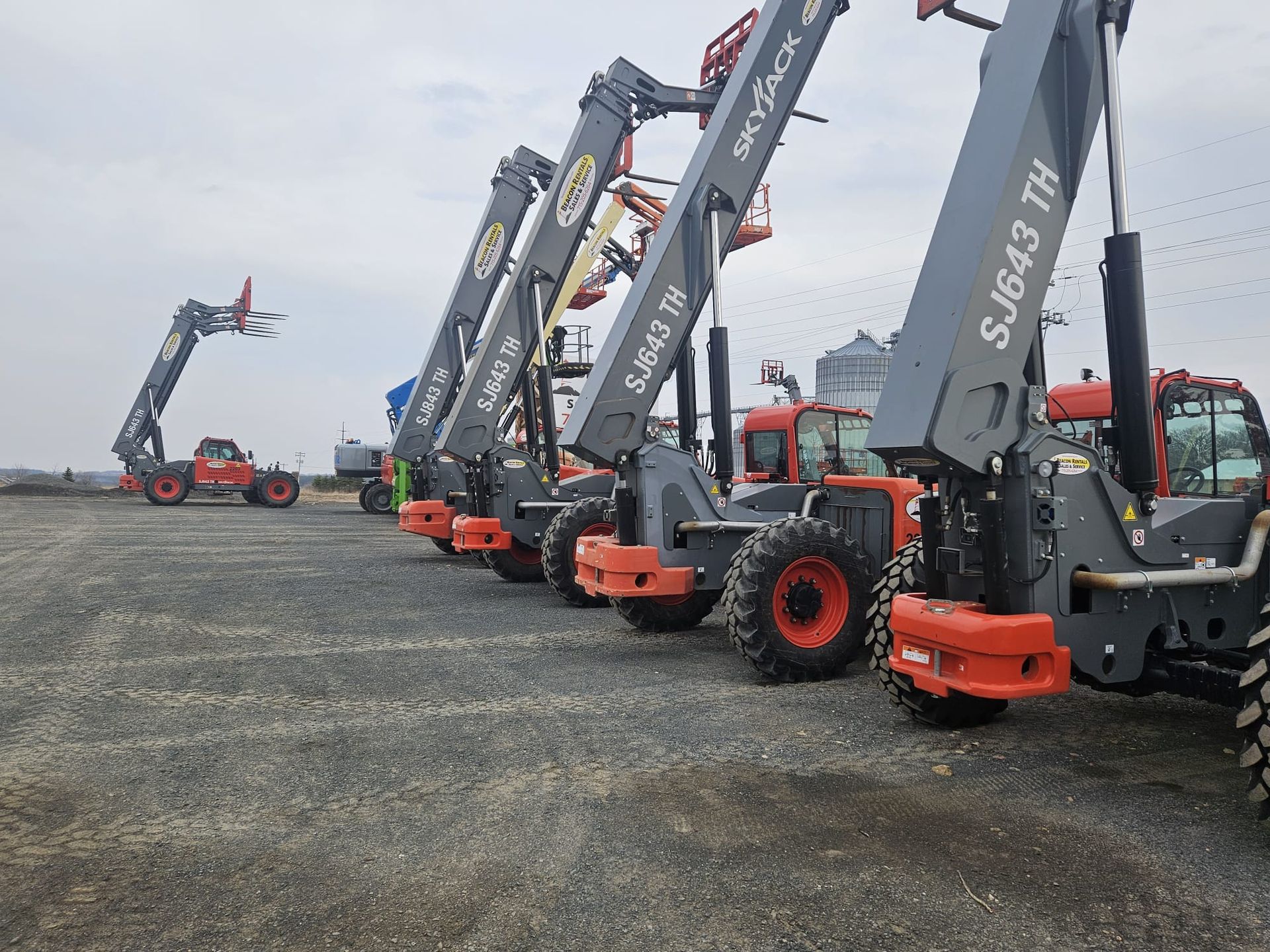 Row of grey Skyjack SJ643 TH telehandlers with red accents on gravel. One in background.